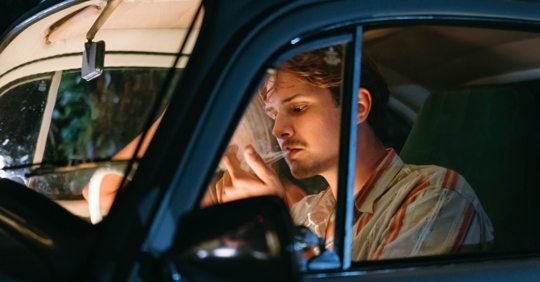 Photo of a male driver lighting an unidentified object to smoke in his car.