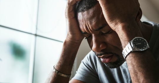 Close up photo of a frustrated man resting his head in his hands.
