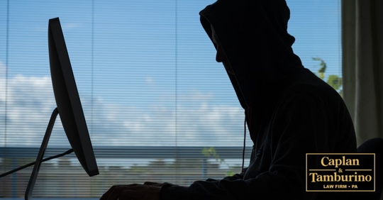 Silhouette of person with hoodie on sitting at a computer.
